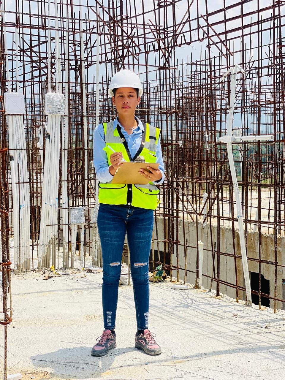 Rosibel Cordero Reyes, ingeniera civil, con casco y chaleco de seguridad supervisando una obra frente a una estructura de acero de refuerzo.